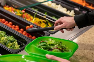 A student fills a to-go container with vegetables.