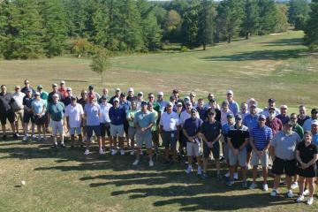 A large group of golfers stand together on the golf course at the Lonsbury Memorial Scholarship Golf Classic