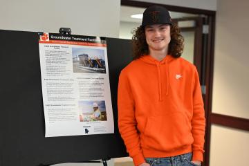 A student stands by his project poster at the ASER Student Summary Project Student Expo 