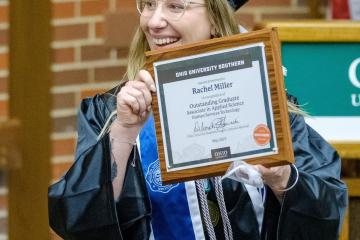 woman in cap and gown holding plaque and smiling