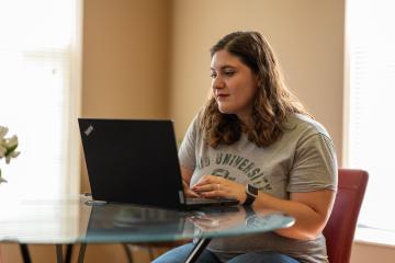 An OHIO Online student works on a computer while sitting at a table