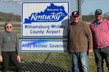 Laurie McKnight, Brent Lane and another individual stand outside, in front of the Williamsburg-Whitley County Airport sign in Kentucky