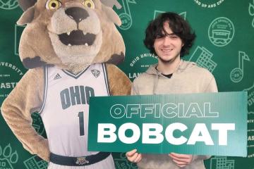 Peyton Wellman holds a sign that says 'Official Bobcat" while he stands next to a cardboard cutout image of Rufus