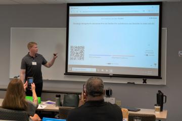 An instructor from the Ohio Center of Excellence for Behavioral Health Prevention  and Promotion points  at a power point screen while leading a class presentation