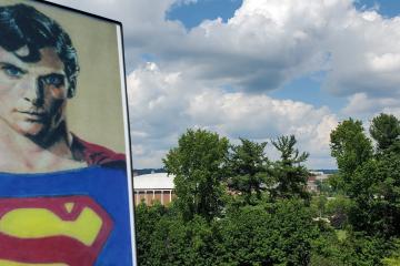 An artistic image of Superman is shown against the Athens skyline, which includes the Convocation Center