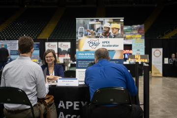 Three individuals talk at an APEX Accelerator table at an event