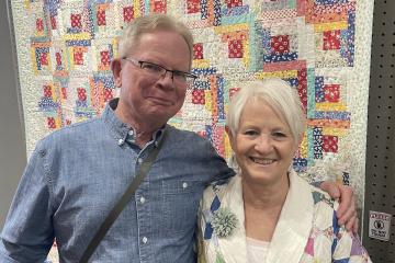 Man and Wife, standing in front of handmaid quilt