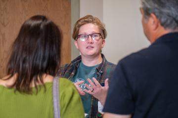 Woman speaks with two people, gesturing with her hands