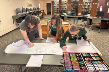 Three students use markers on large posterboard