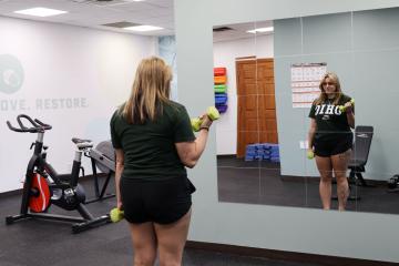 Blonde female looking in a mirror in a fitness room, lifting weights