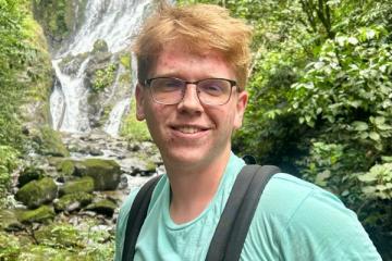 Student with glasses in front of waterfall with backpack