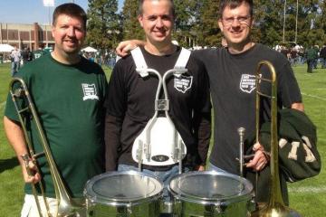 The Voytek brothers stand together with their musical instruments while wearing Marching 110 Alumni clothing items