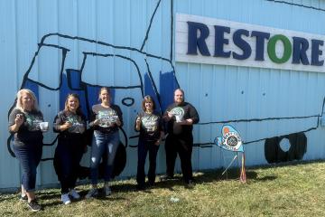 OUCU employees stand in front of a mural painted on the ReStore building