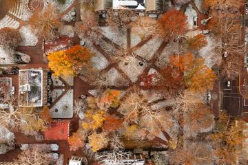 The College Green is shown with snow on the ground and colorful Fall leaves on the trees in this aerial image.