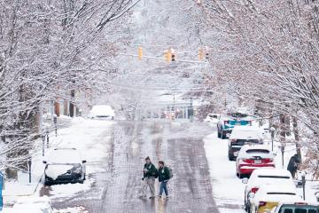 Two OHIO students walk across a street while the cars near them and the trees above them are covered in snow
