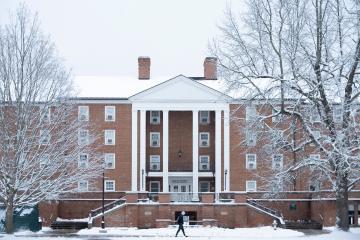 An OHIO building and the trees near it on the South Green are covered in snow. A student walks in front  of the building