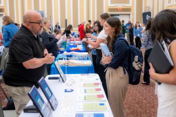 An OHIO student talks with a business representative, while many other students are also shown in the background talking with business representatives at the Career Fair in the Baker University Center Ballroom.