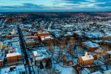 A drone image of Ohio University's Athens Campus, including Cutler Hall and the College Green, with the city of Athens in the background and clouds in the sky