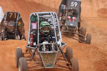 Baja car driving forward (toward camera) as three trail behind. 