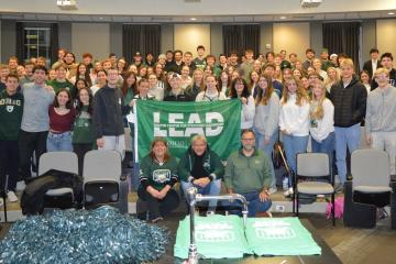 A large group of OHIO students and employees stand with Bas Baalmans and hold a green flag that says "LEAD"