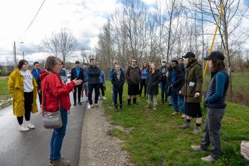 An OHIO faculty member talks to a group of students while standing outside on a paved bike path or small road, while some students stand in the grass