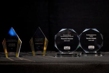 Several faculty awards are displayed on a table, including awards for Pamela Kaylor, Sarah Wyatt and Adam Rapp