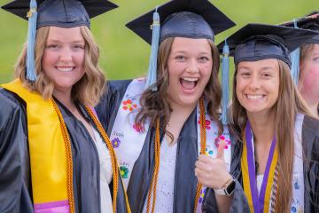 Three OHIO graduates smile together while wearing their caps and gowns, standing outside after the Graduation Recognition Ceremony at Ohio University Lancaster