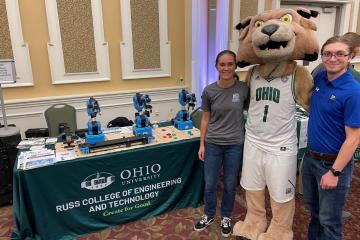 Brandon Petrie stands next to Rufus the mascot and another OHIO student and next to a Russ College of Engineering and Technology booth 