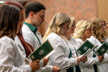 Row of students in white coats looking at program during pinning ceremony