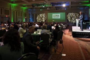 John Carey speaks in front of a large crowd in the Baker University Center at the State of the Region Conference