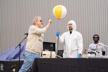 An OHIO faculty member pokes at a beach ball as part of an science exhibit,  while two other OHIO representatives look on  at the Science Day event