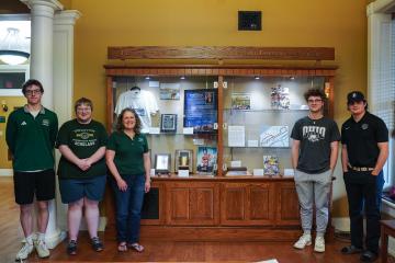 OHIO students and a faculty member stand in front of a display case showing some of the Voinovich Archives items