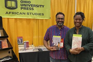 Jody Benjamin and Ademide Adelusi-Adeluyi hold their books and stand by a banner that says "Ohio University Press - African Studies"
