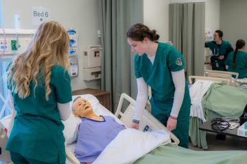 Students in scrubs attend to manikin in hospital bed