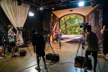 High School Media workshop participants take video and watch other production equipment while a musician plays a guitar on a set for a video