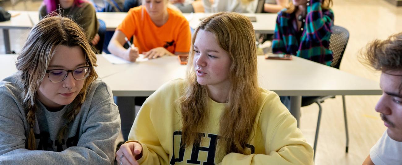 Two students sitting at a table talking to each other