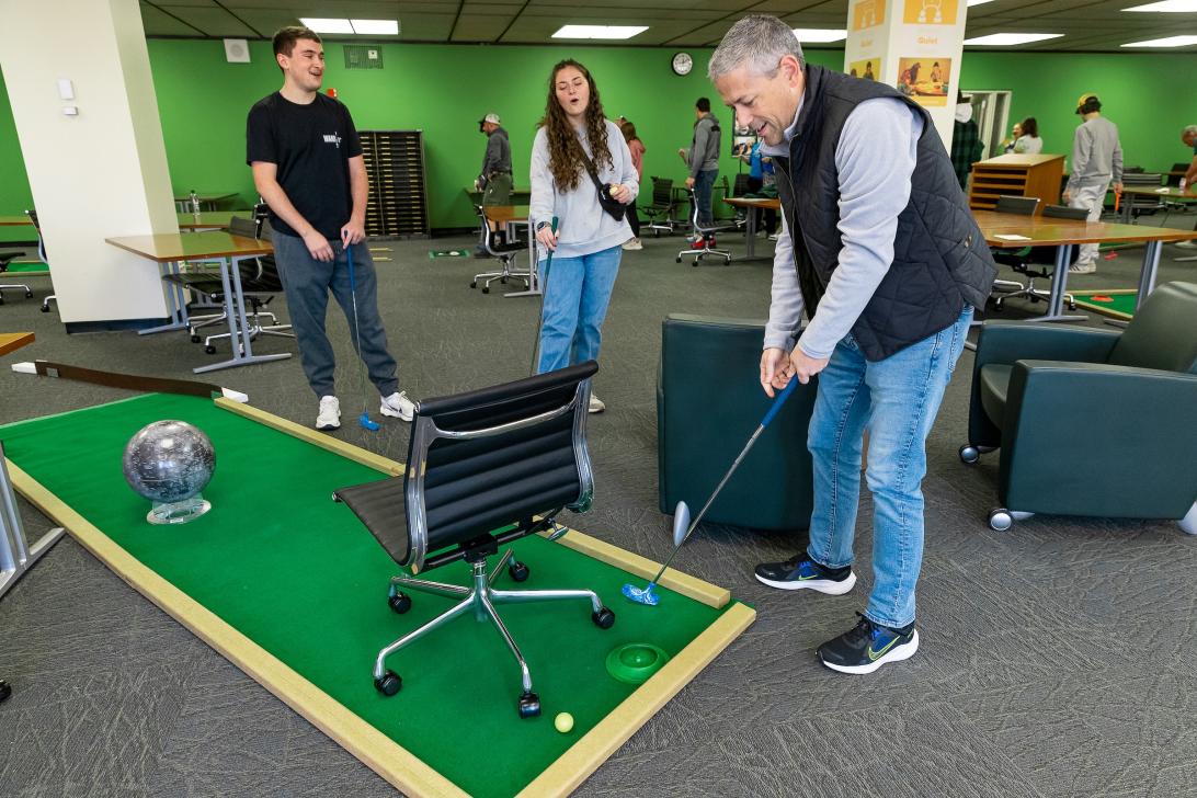 2 students and their parent playing golf in Alden Library 