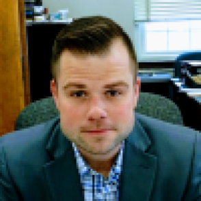 brad peoples headshot: Caucasian man sits in an office wearing a gray suit jacket and patterned dress shirt.