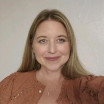 Headshot photo of a smiling woman with long, straight blonde hair and an orange sweater. 